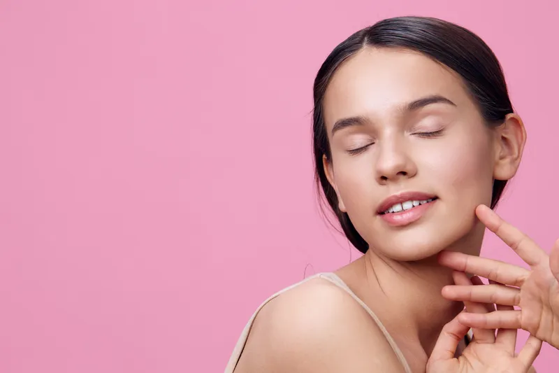 Young woman with closed eyes smiling against a pink background, showcasing natural beauty and tranquility Perfect for beauty, skincare, and lifestyle themes