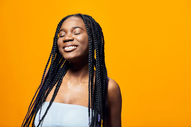 Young Black woman with braided hair smiles joyfully against a vibrant yellow background, showcasing confidence and happiness in a bright, seasonal portrait