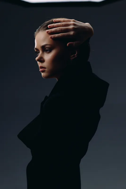 thoughtful woman in black turtleneck with hand on head against dark background