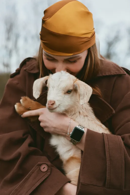 goat kid woman holding animal affection outdoors lifestyle scene, warm coat embrace against a snowy backdrop, conveying tenderness companionship rustic charm and gentle bonding suitable for family