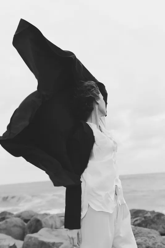 Windy beach scene with flowing scarf over light clothing, ocean horizon behind, dynamic movement, dramatic mood, outdoor freedom and coastal exploration