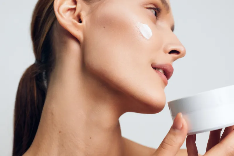 Young woman applying face cream on cheek closeup, skincare routine, smooth skin, natural beauty, soft light, healthy lifestyle, gentle moisturizing, clean background
