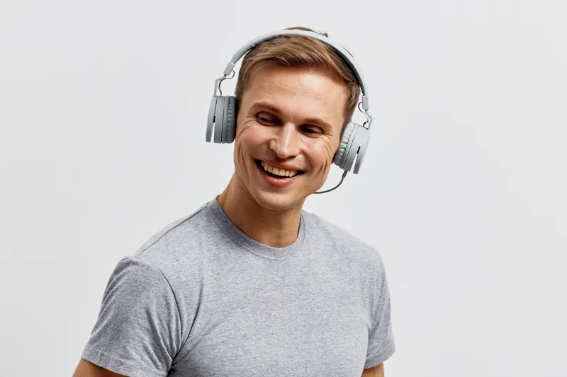 Smiling young caucasian man wear headphones gray t-shirt look side listen music digital nomad lifestyle isolated white background studio portrait