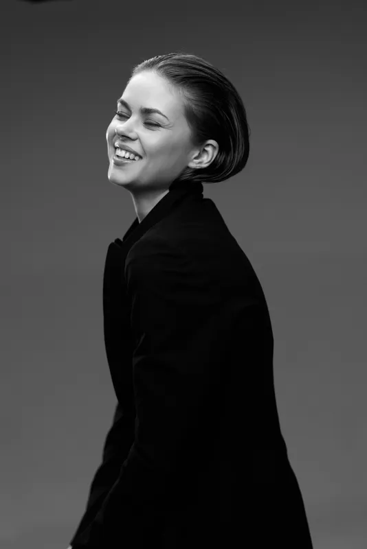 Smiling woman in black jacket captured in black and white studio portrait with joyful expression