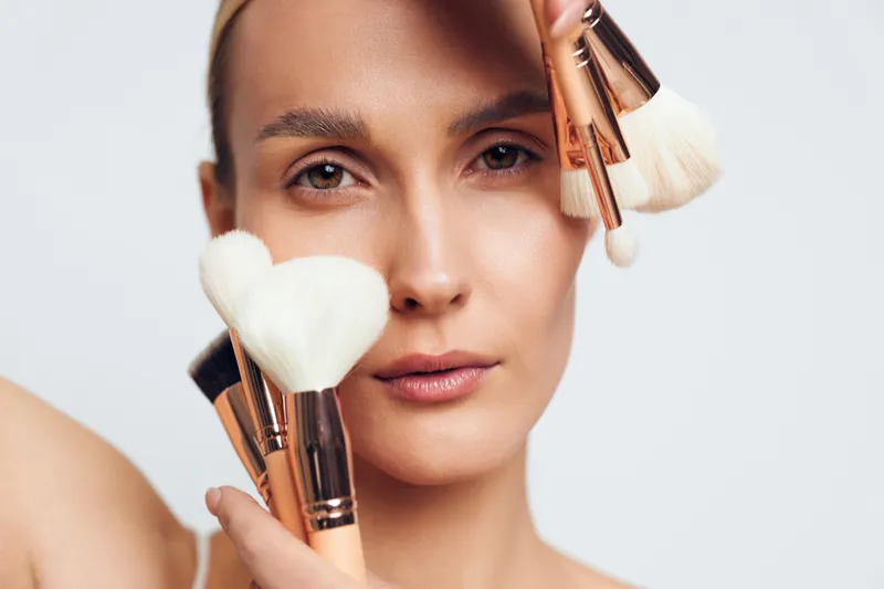 Woman makeup brush closeup beauty cosmetics portrait studio, soft natural light, applying foundation on smooth face, calm professional grooming in clean skincare routine