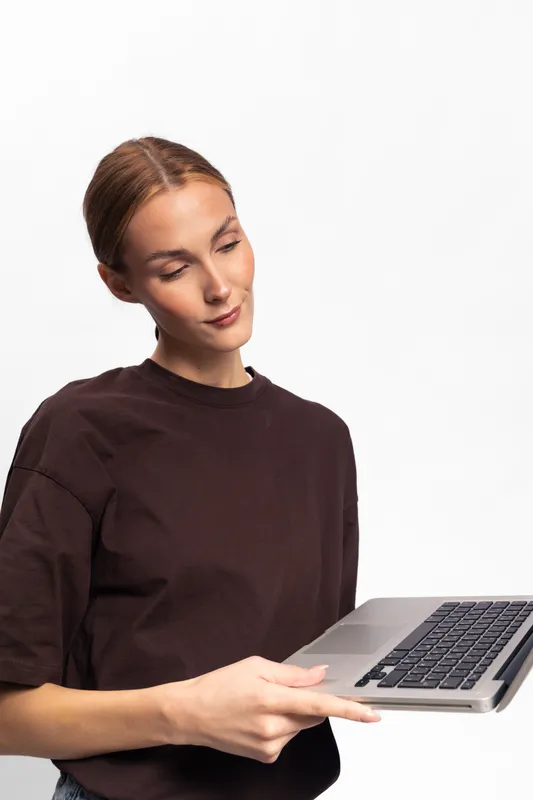 Young woman in brown shirt holding open laptop looks at screen with slight smile isolated on white background. Concept for technology, work, and casual lifestyle.