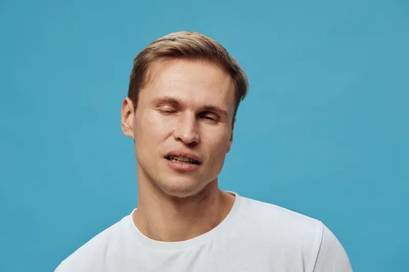 frustrated young caucasian man wearing white t-shirt eyes closed expressing stress isolated on blue background mental health gadget concept