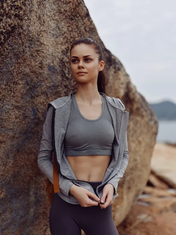 Young athletic woman in sportswear, standing confidently against a rocky background, conveying strength and determination in an outdoor setting