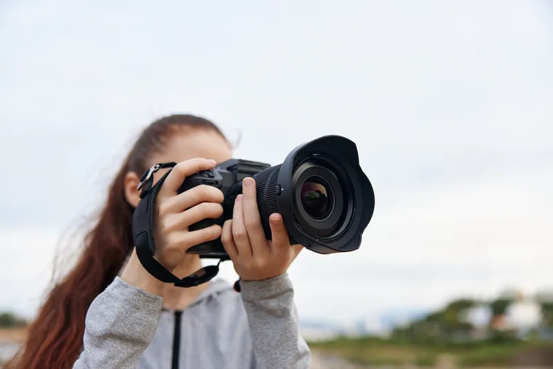 A young female photographer capturing nature with a DSLR camera, dressed in casual sportswear, showcasing a focused expression in a serene outdoor setting
