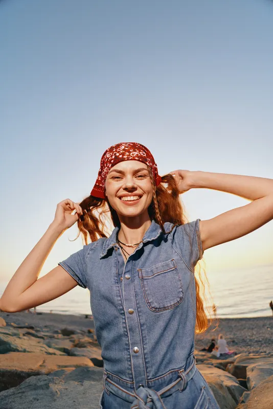 Lifestyle woman wearing modern boho-western denim street style smiling outdoors at sunset, film color capturing natural joy and free spirit in casual outfit.