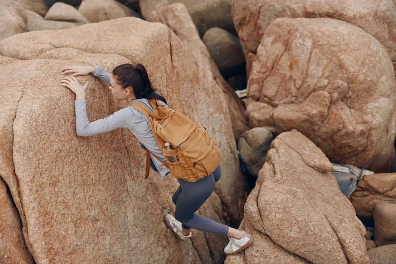 Young woman climbing rocky terrain with a backpack, showcasing adventure and determination in an outdoor setting Perfect for fitness and outdoor lifestyle themes