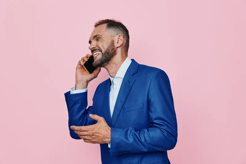 A confident business professional on a pink backdrop talks on a phone, exuding energy and polished style. The isolated color highlights focus, ambition, and clear communication in a dynamic portrait.