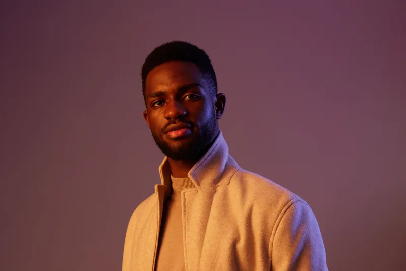 Confident young black man in stylish beige jacket against a purple background, exuding a modern and sophisticated vibe KEY confident, young, black, man, stylish, beige, jacket, modern, sophisticate