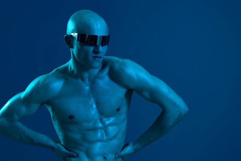Athletic man with sunglasses showcases a strong physique in a blue-toned, high-contrast black and white image, emphasizing strength and confidence.