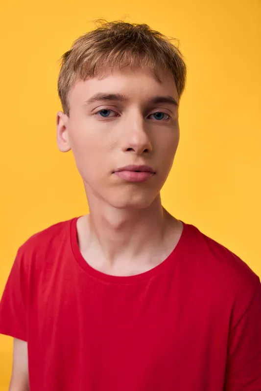 Youth, male in red shirt, studio setting with yellow background, neutral expression, soft lighting, clean composition, headshot style for contemporary fashion stock use