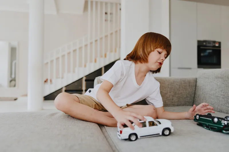 Young boy playing with toy cars, enjoying indoor leisure, bright atmosphere, home setting, engaging activity.