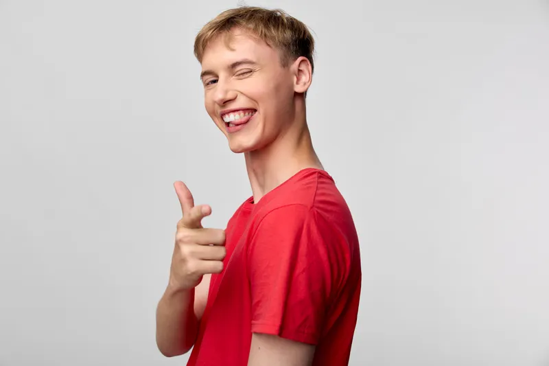 Man, smile, red shirt, pointing gesture in a casual studio setting for stock photography, bright dynamic friendly vibe suitable for advertising, lifestyle or marketing campaigns
