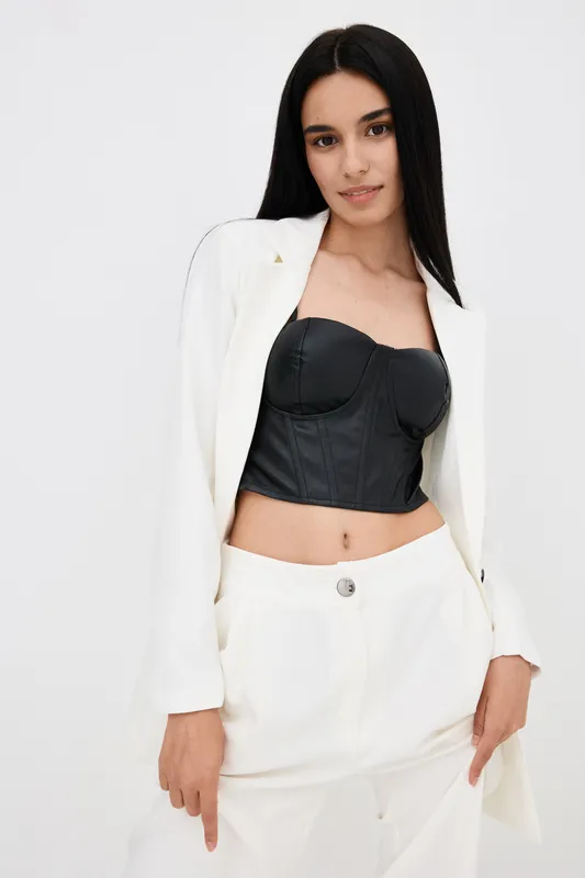 young woman with long black hair wearing stylish white suit and black corset top posing confidently against white background in studio setting