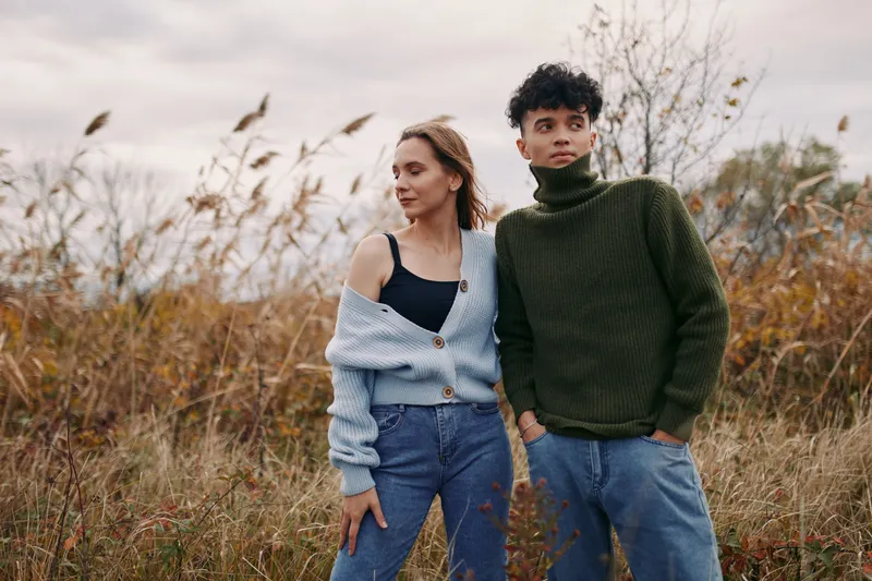 Candid portrait of a young couple standing in tall grass, conveying genuine connection and believable interaction with natural expressions, relaxed posture and warm earthy tones.