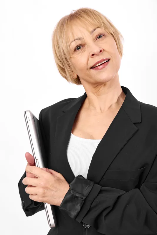 Senior woman portrait, blonde short hair, smiling in black blazer, holding notebook folder on white background, business professional, friendly studio shot, vertical view