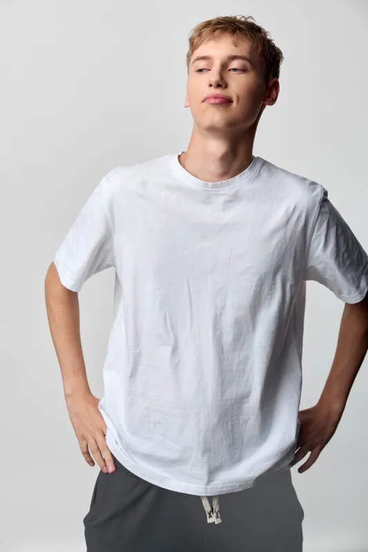 Casual male model in a plain white t shirt stands in a studio, confident pose with hands on hips, soft lighting and minimalist wardrobe suitable for fashion and lifestyle shoots