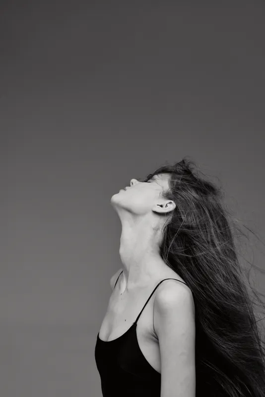 Black and white portrait of a woman with long hair in a tank top looking upward, expressing freedom and elegance.