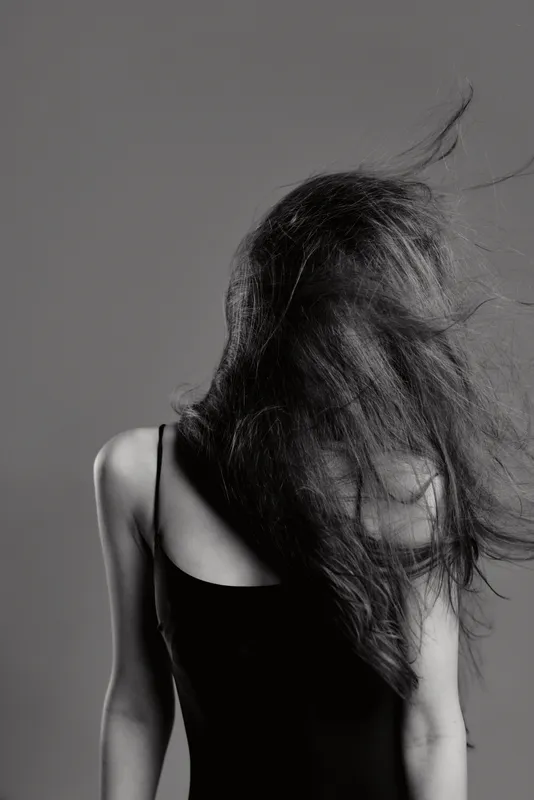 Black and white portrait of a woman with long hair flowing, wearing a black dress, emotional and mysterious atmosphere.