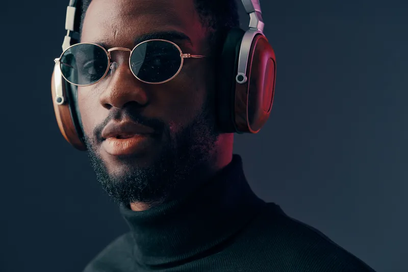 Young man with sunglasses and headphones, wearing a stylish turtleneck, exuding confidence against a dark background, perfect for music and fashion themes