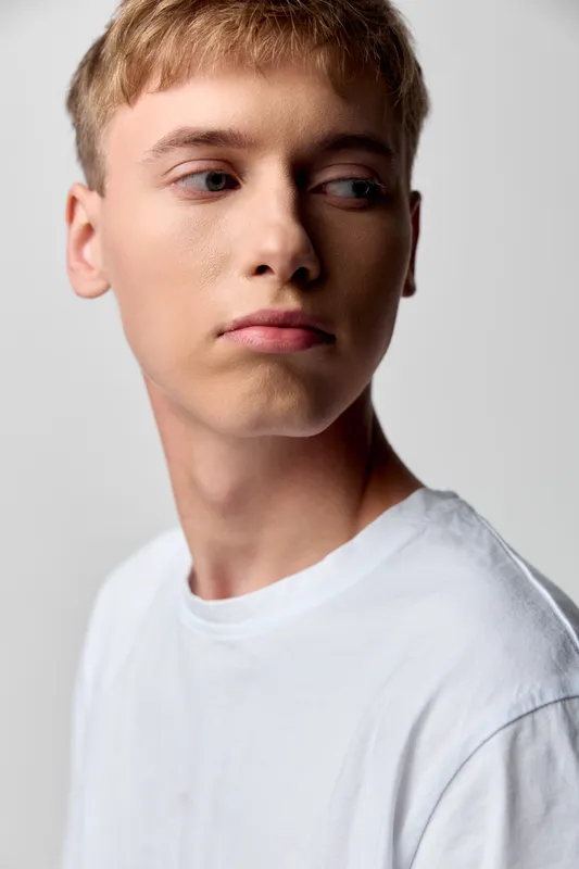 Young man side profile thoughtful casual white t shirt studio lighting neutral background studio backdrop expression calm lighting male model in a clean fashion shoot
