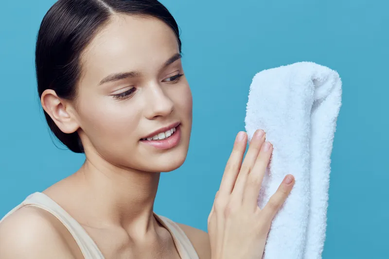 Young woman with a towel, smiling and looking relaxed, representing skincare and wellness, against a soothing blue background