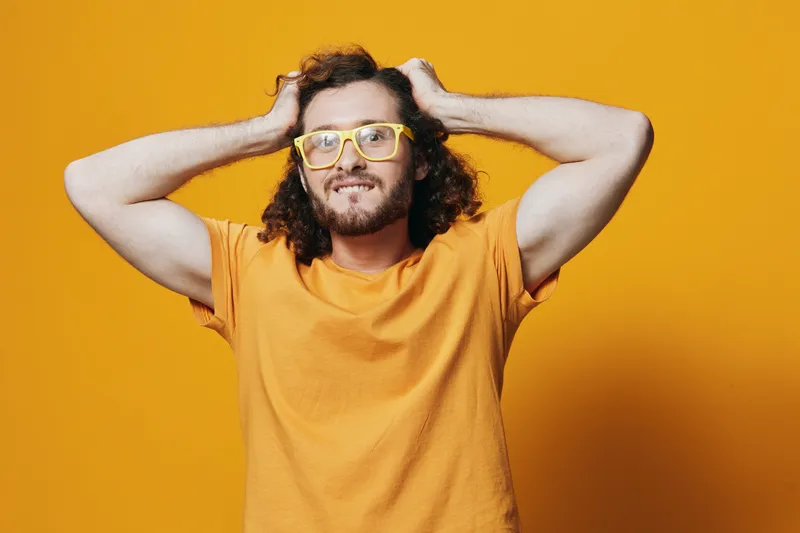 Young man with curly hair expressing joy in a vibrant orange shirt against a bright yellow background, ideal for creative and cheerful themes