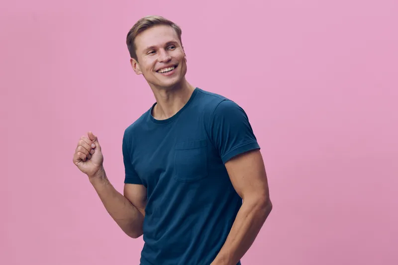 smiling man in blue t-shirt look side happy gesture digital nomad work lifestyle casual wear pink background studio portrait concept