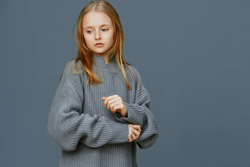 Thoughtful young girl in a cozy gray sweater, featuring a neutral background, showcasing introspection and calm emotions in a seasonal winter setting