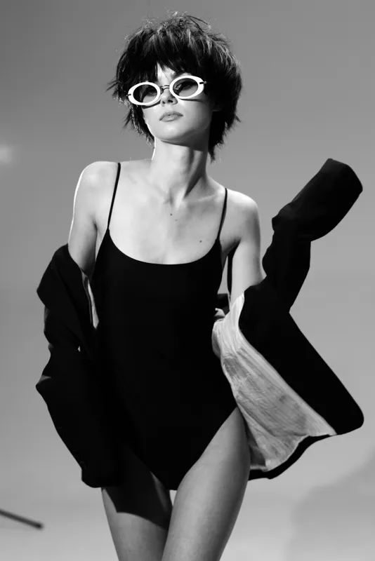 Black and white stylish woman wearing sunglasses and swimsuit with an open jacket, confident and modern look