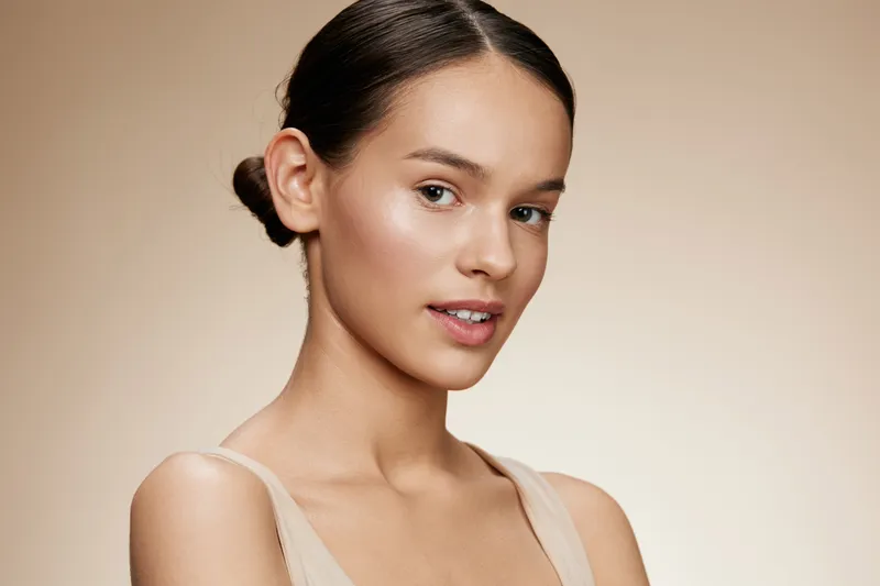 A serene young woman with a natural look showcasing healthy skin and minimal makeup, highlighting beauty and confidence in a soft beige background