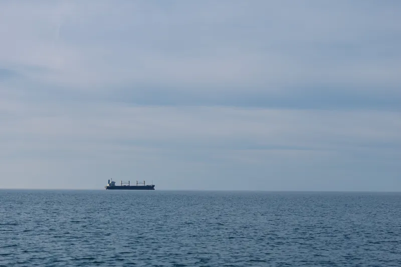 Calm sea and distant cargo ship on the horizon, vast water under a cloudy sky in a maritime scene, a lone vessel drifting across the ocean blue.