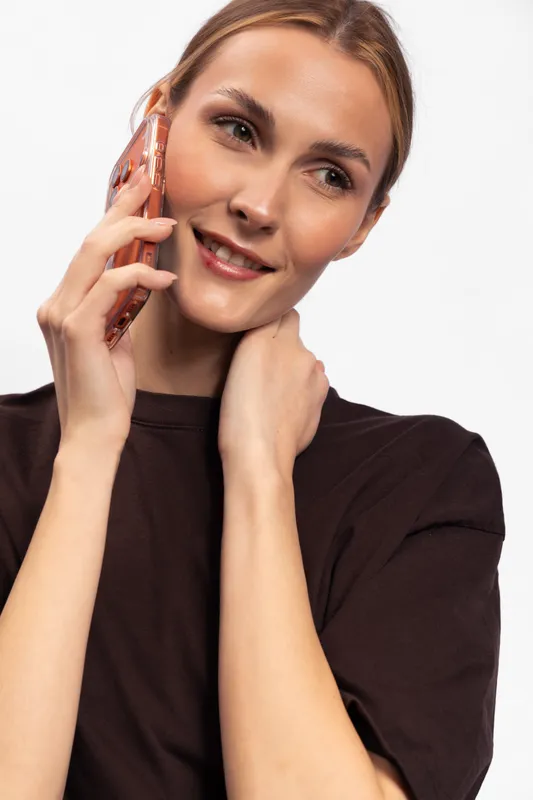 Smiling young woman with clear skin talks on smartphone, wearing dark top. Studio portrait on white background. Concept of communication, technology, and positive emotions.