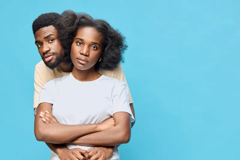 Young black couple expressing love and intimacy against a vibrant blue background, showcasing natural hair styles and casual attire