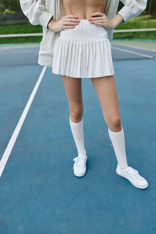 Young woman in a sporty outfit, exuding confidence on a tennis court in a pleated skirt and socks, showcasing an active and vibrant lifestyle
