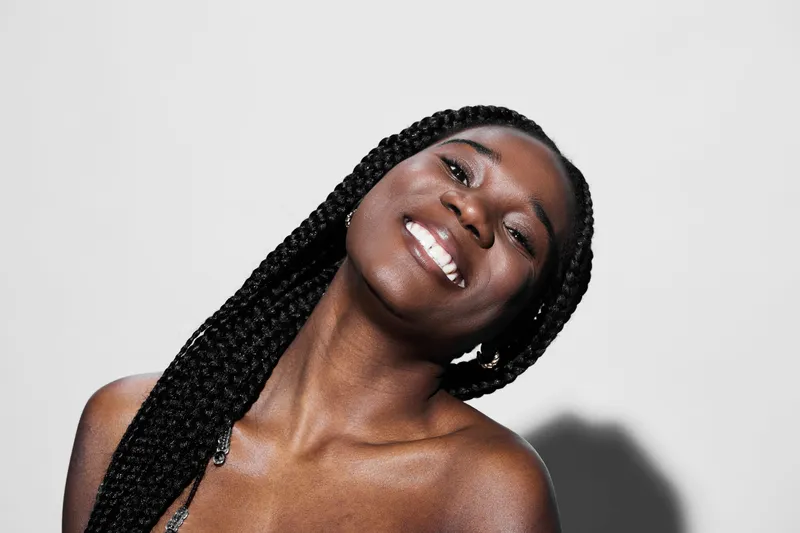Joyful young woman with braided hair showcasing a radiant smile, ideal for health and beauty concepts, featuring a clean, minimalistic background