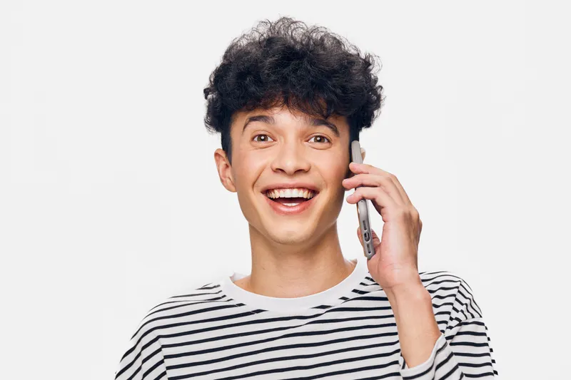 smiling man talking on phone wearing striped shirt, cheerful expression, curly hair, isolated on white background, casual and bright portrait