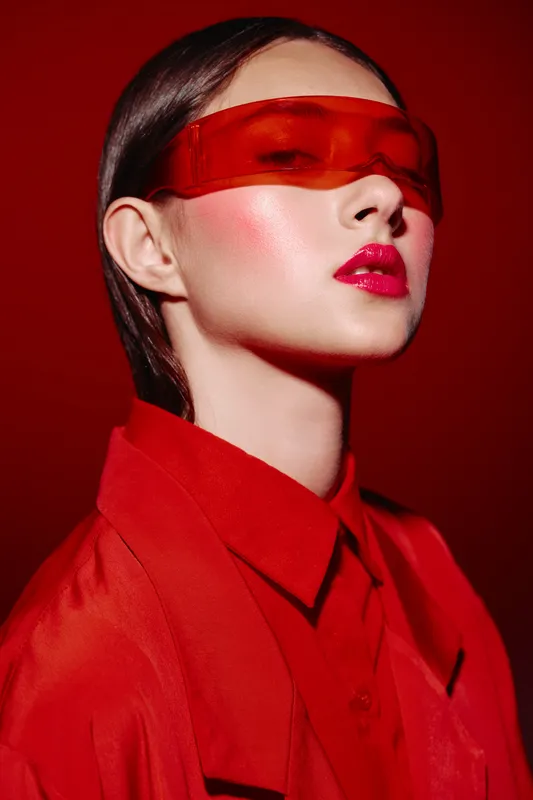 Close-up portrait of a fashionable woman with glossy red lips and red visor sunglasses, wearing a red jacket, on a red background. Creative beauty and fashion art concept.