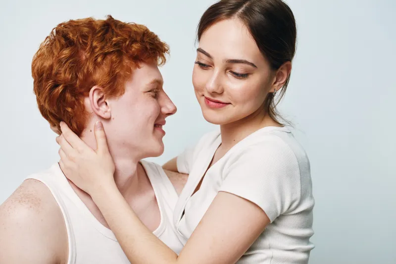 Young couple embracing and looking at each other with affection in studio. Woman holding man’s neck, closeup with soft expressions and gentle connection between lovers.
