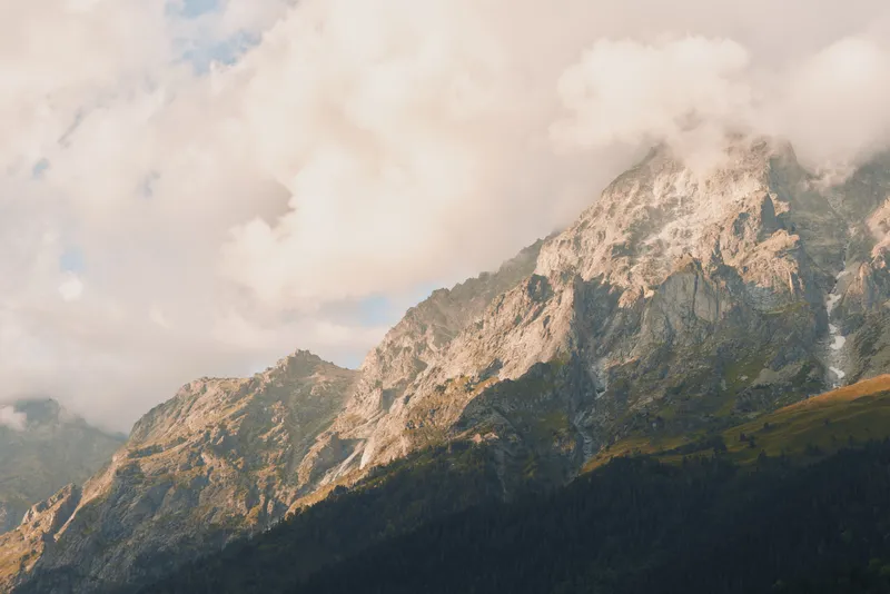 A lone hiker gazes at rugged mountain peaks as clouds drift above a sunlit valley, capturing a calm outdoor moment of nature, solitude, and self reflection