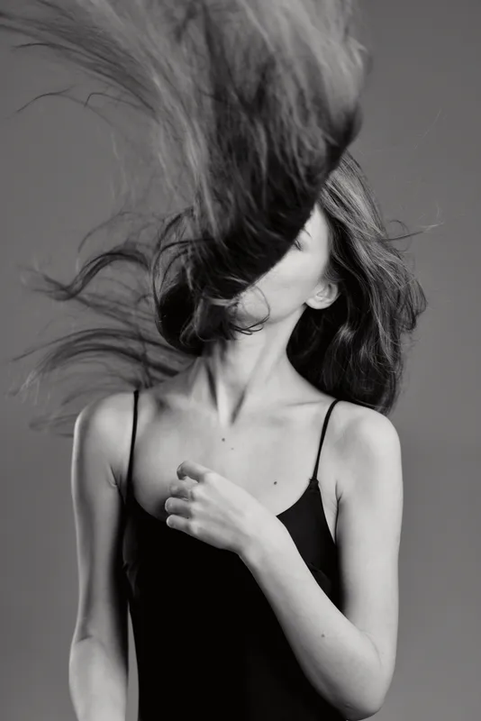Black and white portrait of a young woman with flying hair wearing a black top, dynamic motion, and minimalistic style.