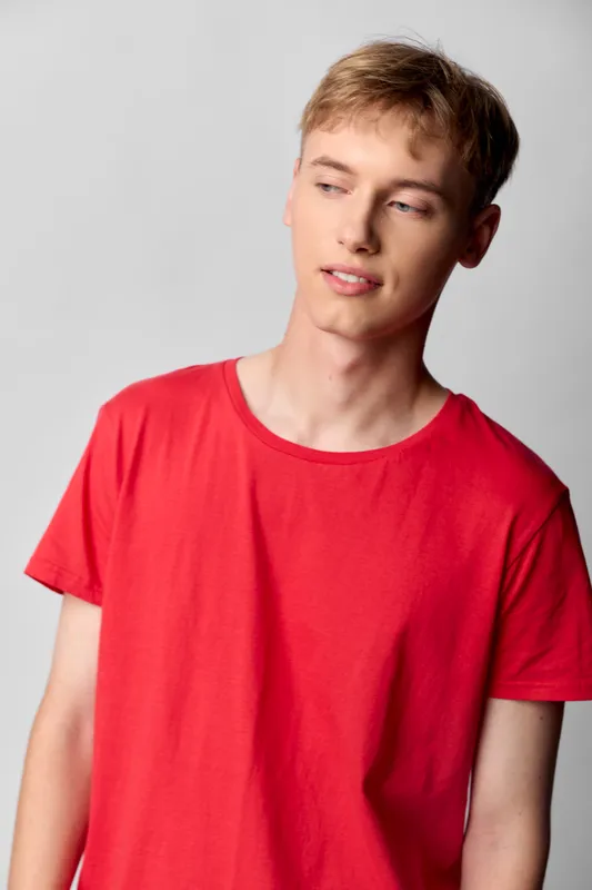 Red t shirt worn by a young man in casual fashion, relaxed pose and soft lighting, simple studio background, everyday style for lifestyle and fashion use, clean minimal composition for product and