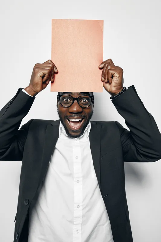 African man with dark skin and glasses holding blank paper above head smiling in black jacket and white shirt on white background for business or presentation.