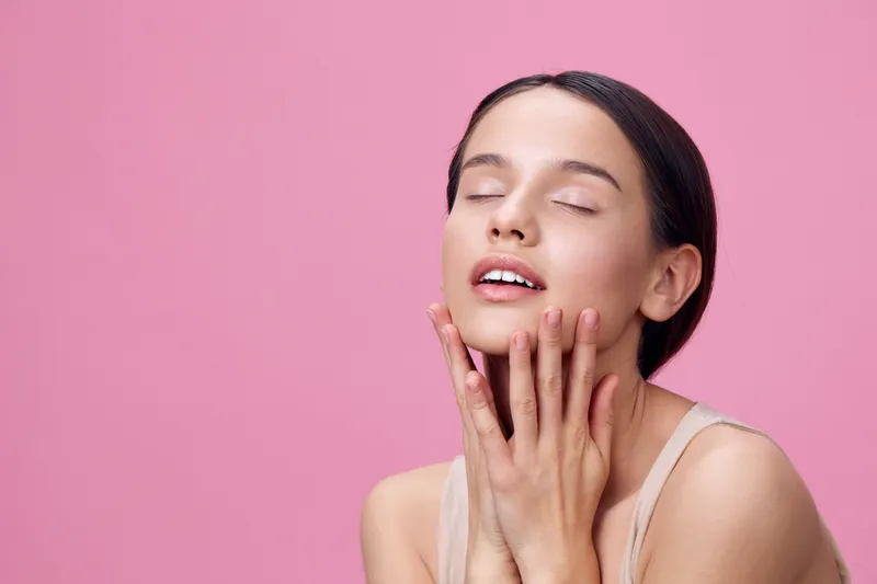 Delicate beauty portrait of a young woman with closed eyes against a soft pink background, showcasing natural skincare and serene emotions, ideal for wellness themes