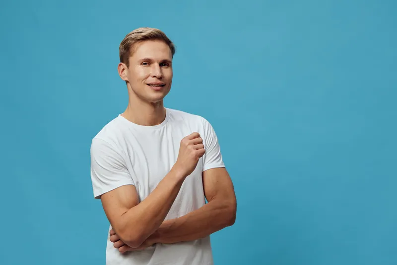 Smiling young man wearing casual white t-shirt looking at camera posing on plain solid blue background studio portrait. People lifestyle concept