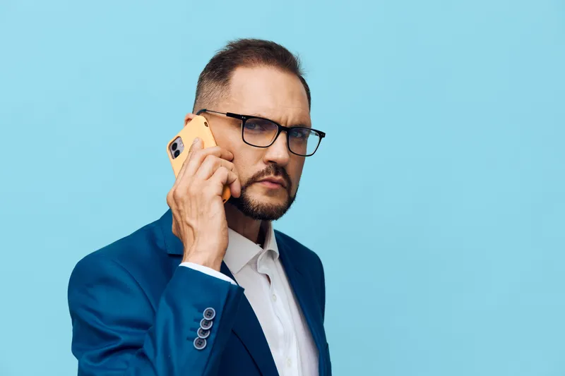 A professional man in a blue suit speaks on a yellow phone against an isolated colored background, projecting confident, focused emotions suited for business, leadership, and corporate use.